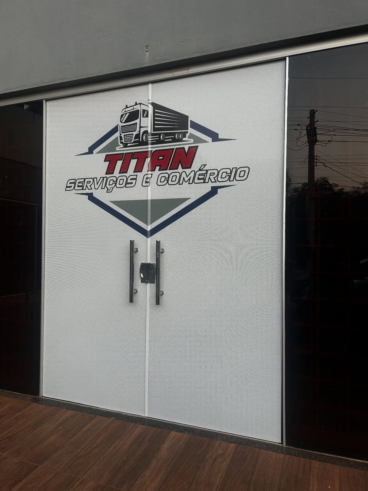 Adesivo aplicado em porta de vidro jateado, que identifica a empresa sem fechar a entrada de luz.