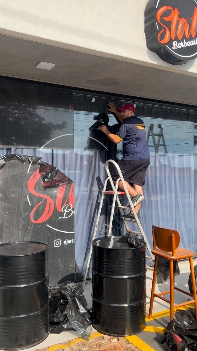 Profissional da Arce sobre a escada aplicando adesivo na vitrine de uma barbearia