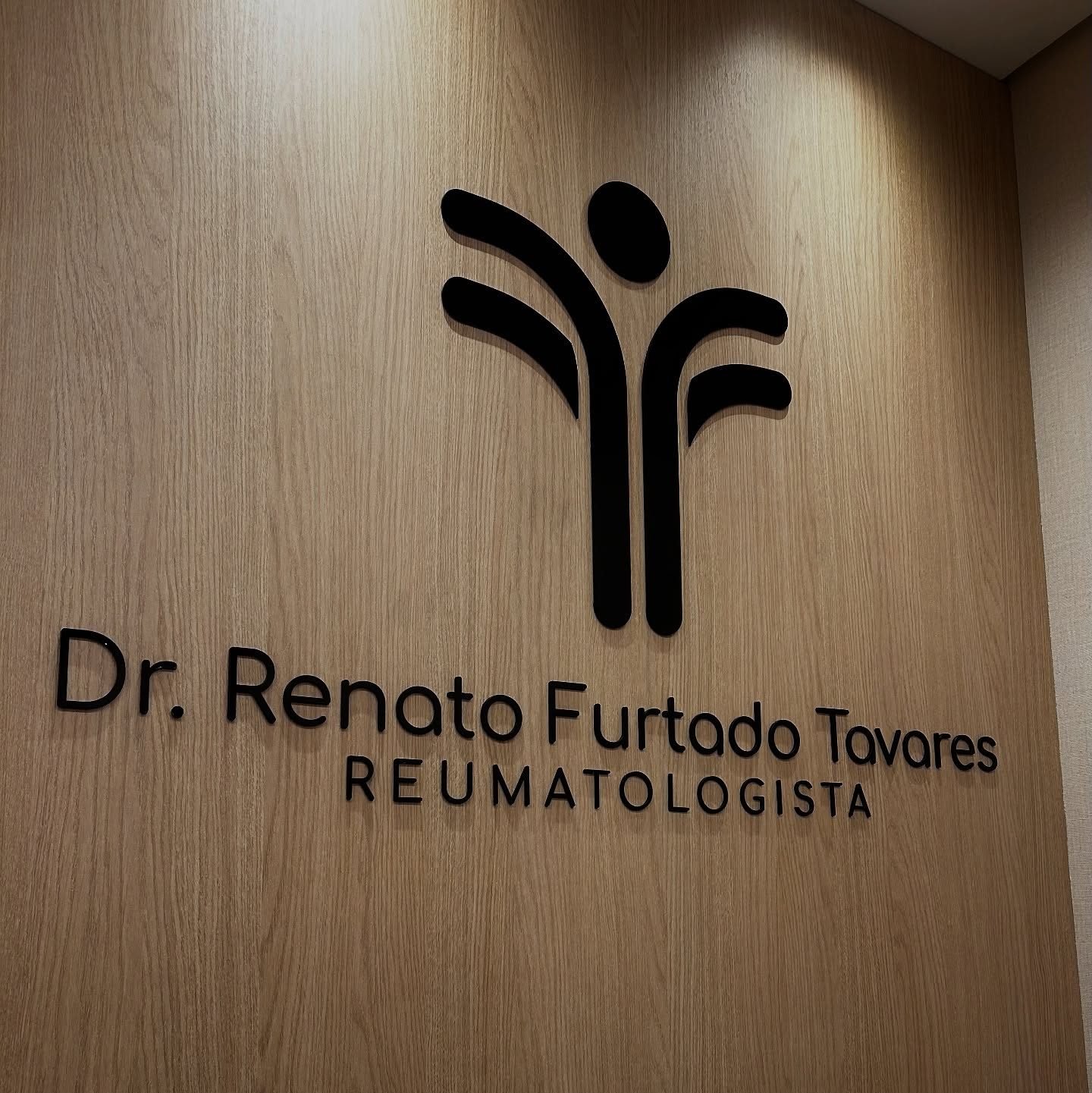 Letra caixa em recorte fino sobre painel de madeira, na parede da recepção do consultório.